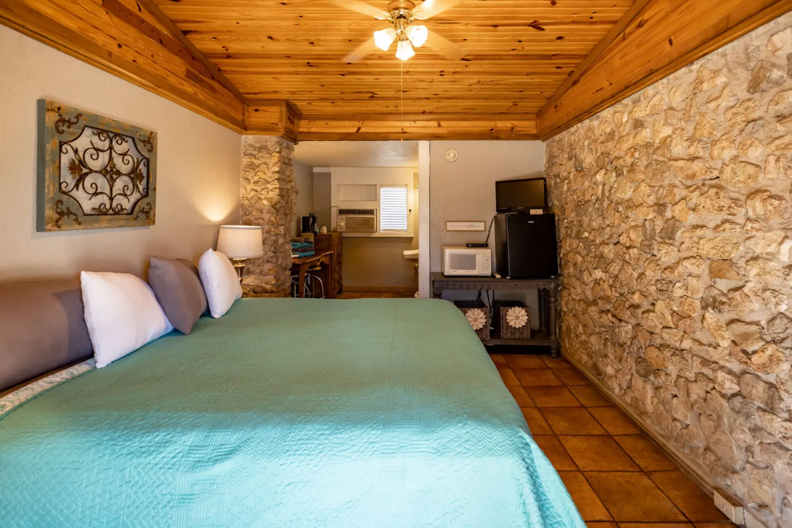 A room with a stone wall design and blue sheets on bed.