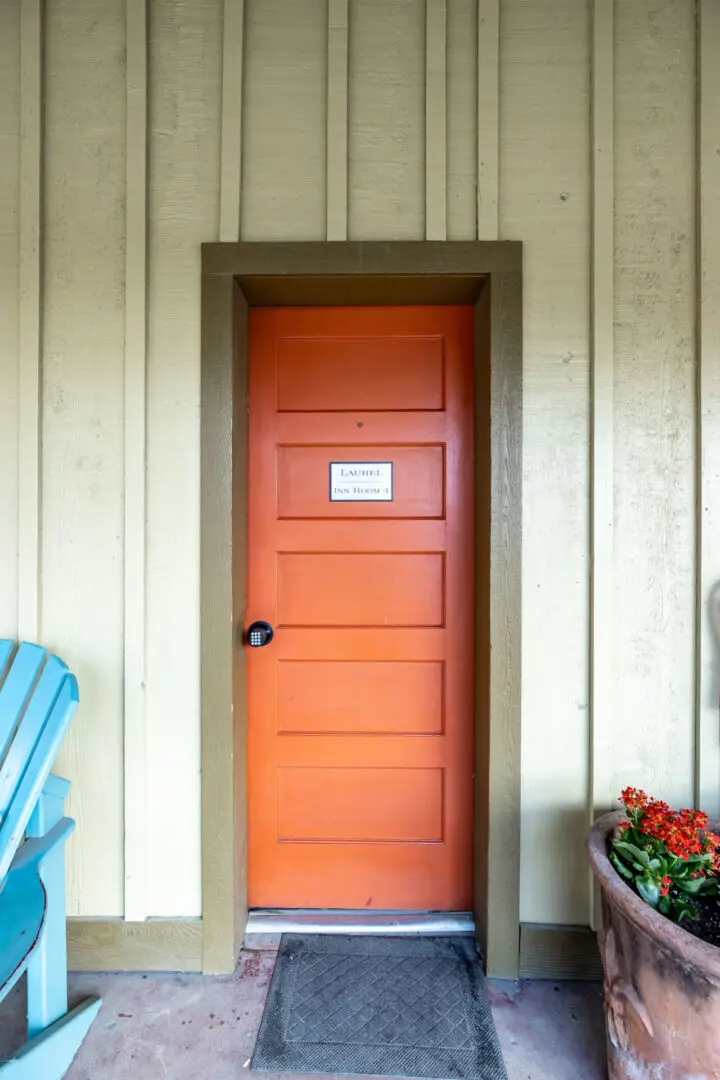 A orange door from the outside with a flower pot on the right side